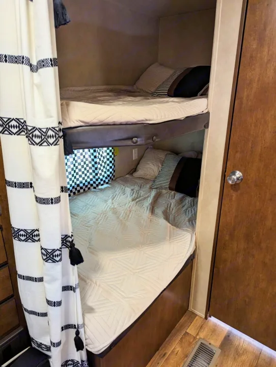 Compact RV rental bunk beds, with soft quilted bedding and decorative curtains, offering cozy sleeping space for travelers.. Forest River Salem 2017