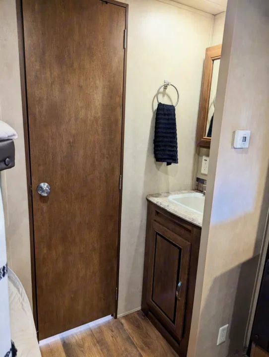 Compact RV rental interior featuring a wood door, sink vanity, towel, and thermostat. Perfect for road trips.. Forest River Salem 2017