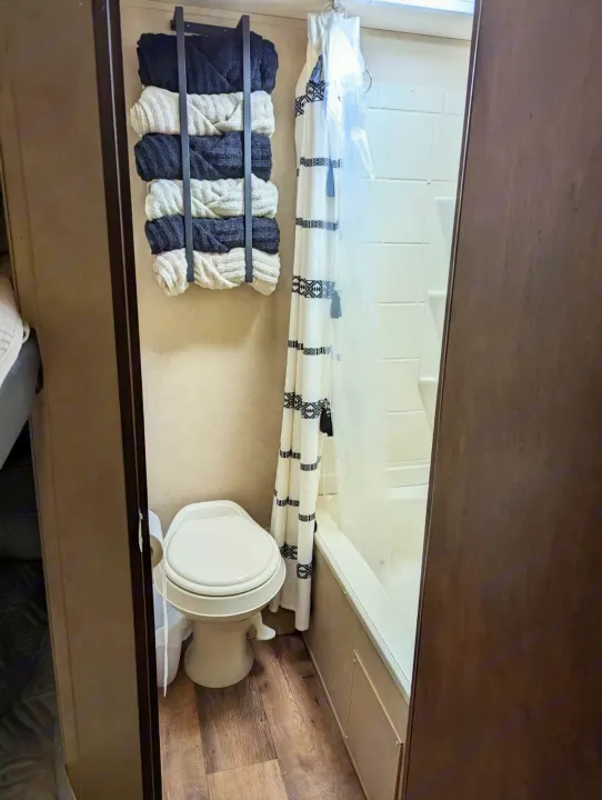 This RV rental bathroom features a toilet, tub/shower with curtain, and wall-mounted towel storage.. Forest River Salem 2017