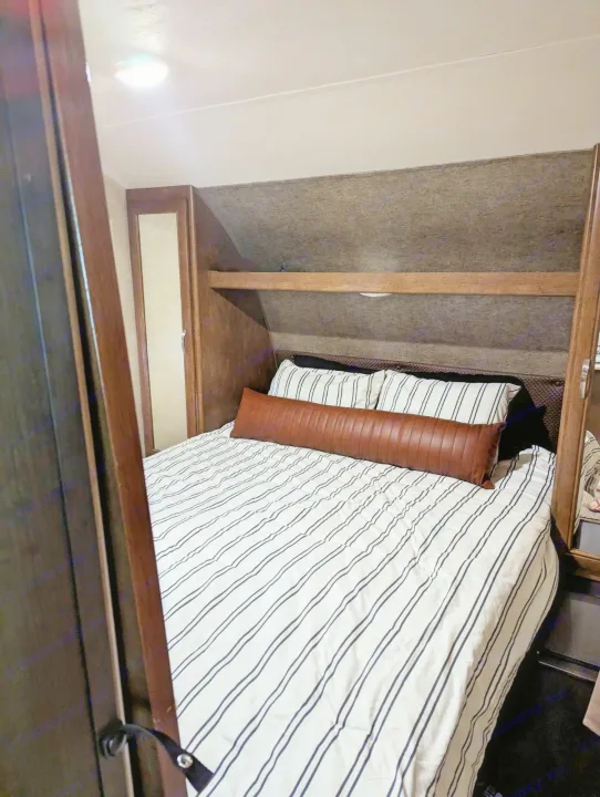 Cozy RV rental bedroom featuring striped bedding, a brown bolster pillow, and built-in wooden storage.. Forest River Salem 2017
