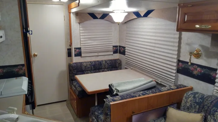 Inside this comfortable RV rental: a cozy dining area with patterned seating, blinds, and warm lighting.. Other Other 2002