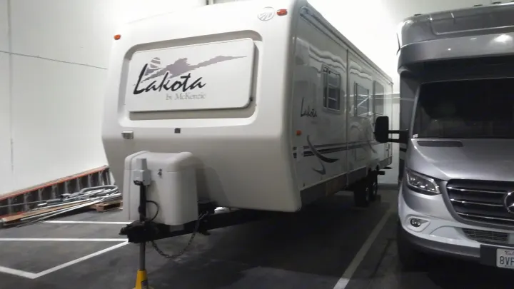White Lakota travel trailer (RV rental) with a silver Mercedes-Benz camper van inside an indoor facility.. Other Other 2002