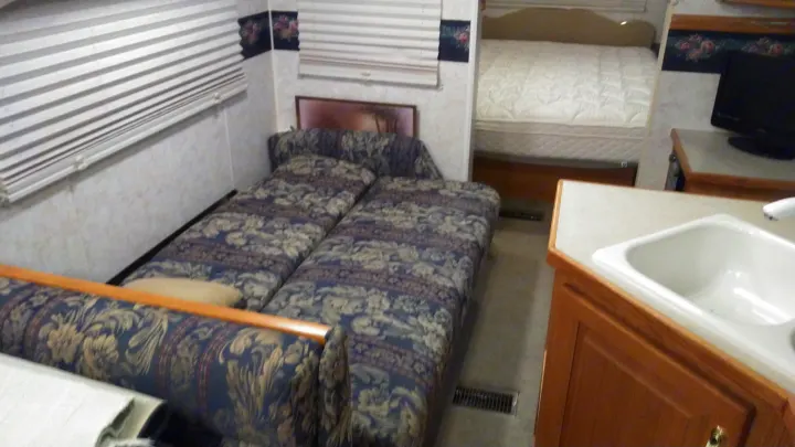 This RV rental interior features multiple beds, a small kitchen area with a sink, and a TV, ideal for travel.. Other Other 2002