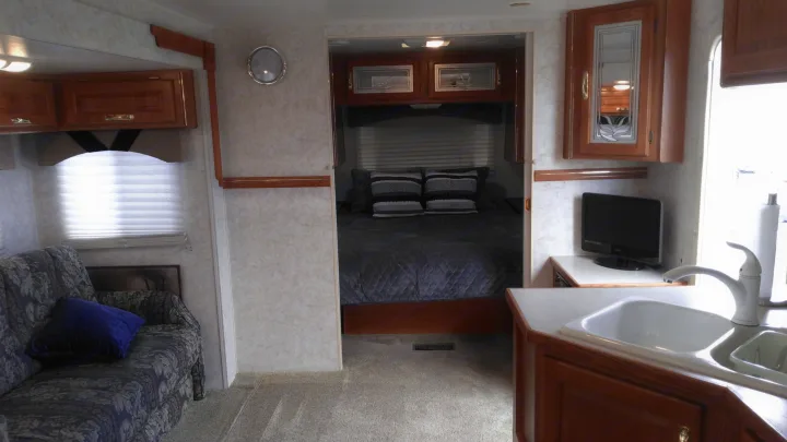 This RV rental features a living area with a patterned sofa, kitchen with sink & TV, and a private bedroom beyond.. Other Other 2002