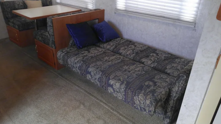 RV rental interior featuring a dinette with a table and bench seating, convertible to a bed, plus a sofa, all with blue floral upholstery.. Other Other 2002