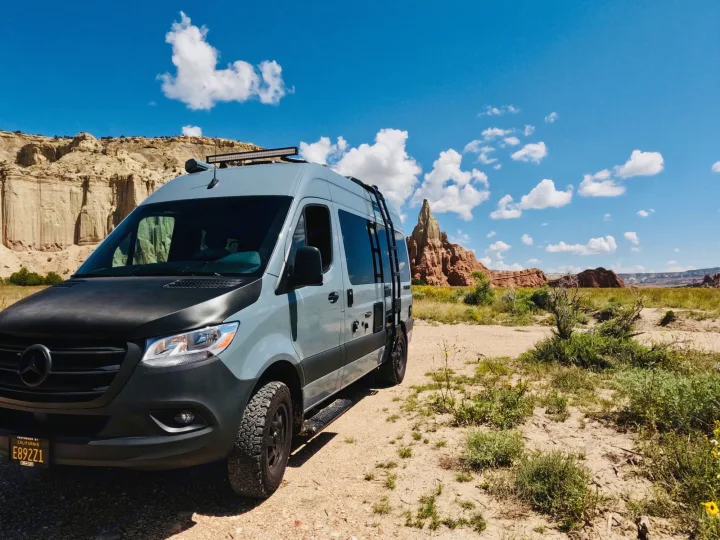 Light grey Mercedes Sprinter RV rental parked on a dirt road, surrounded by desert vegetation and towering rock formations.. Synergy Mercedes-Benz Sprinter 2022