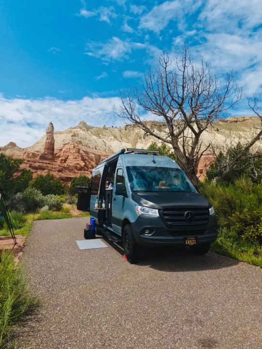 Grey Mercedes Sprinter rv rental van with side door open, parked on pavement amidst unique red rock formations under a blue sky.. Synergy Mercedes-Benz Sprinter 2022