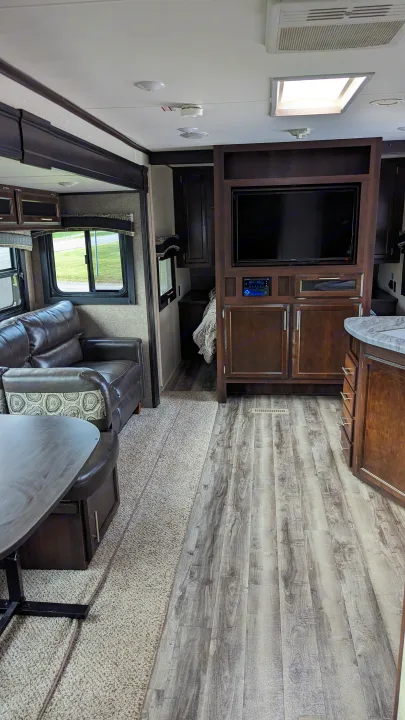 Modern RV rental interior showcasing a living area with dark leather couch, TV, and contrasting wood & carpet flooring.. Jayco Jay Flight 2019