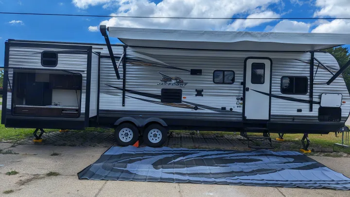 Jayco RV rental with outdoor kitchen, extended awning, and large ground mat, set up for camping comfort.. Jayco Jay Flight 2019