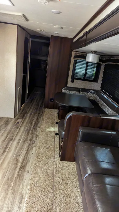 Spacious RV rental interior with a dark wood dinette, brown leather couch, and mixed wood/carpet flooring.. Jayco Jay Flight 2019