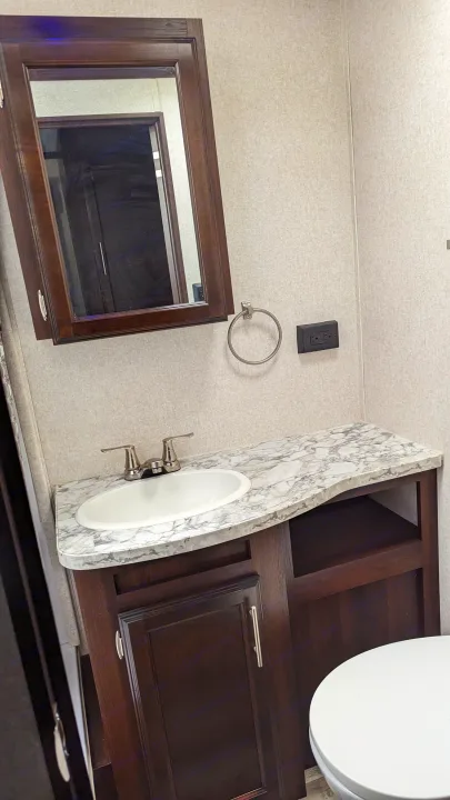 Clean RV rental bathroom features a dark wood vanity, white sink, wall mirror, and partial view of toilet.. Jayco Jay Flight 2019