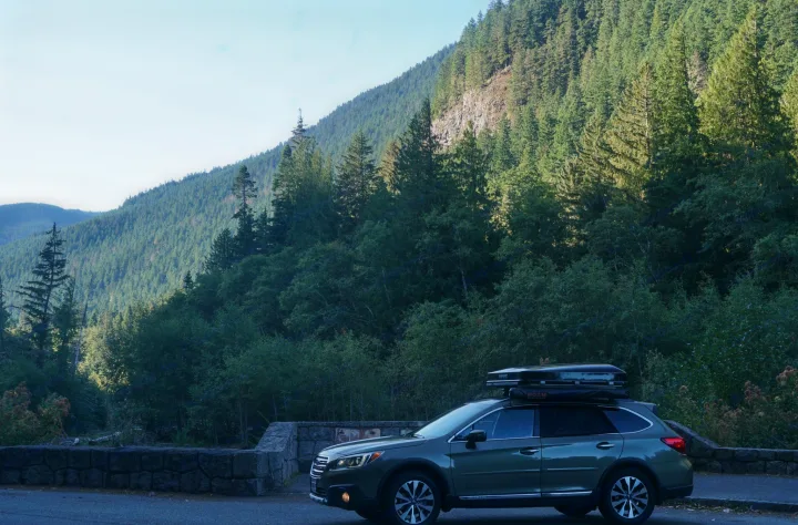 Green Subaru Outback with rooftop tent on a mountain road. Perfect for outdoor adventure & travel, an alternative to RV rental.. Subaru Outback with iKamper 2017