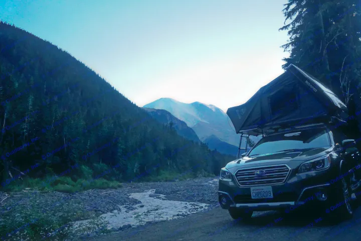 Compact RV rental: Subaru Outback with an iKamper rooftop tent by a river and mountain scenery at dusk.. Subaru Outback with iKamper 2017