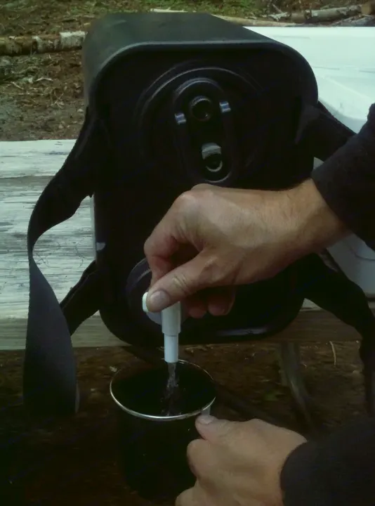 Hands operate a spigot on a portable water tank, filling a cup. Essential for an RV rental camping trip.. Subaru Outback with iKamper 2017