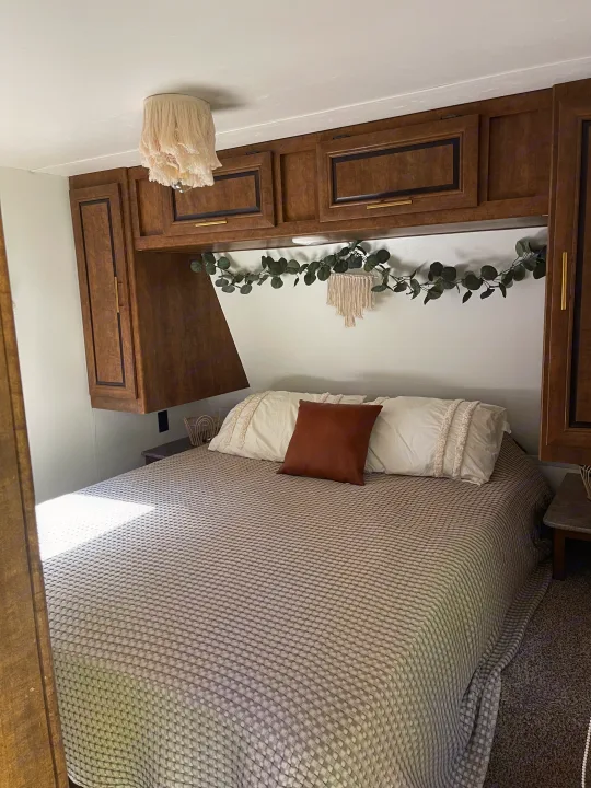 Cozy RV rental bedroom featuring a patterned bed, dark wood storage cabinets, and boho decor.. Crossroads RV Zinger 2017