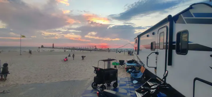 Beachside rv rental with a stunning sunset over the water and lighthouse. Kids play on the sand.. Crossroads RV Sunset Trail Super Lite 2021