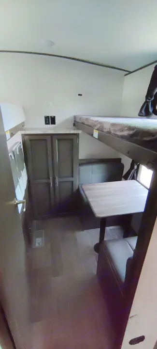 Inside this RV rental, a cozy bunk bed sits above a dinette with bench seats and a table. Storage cabinets nearby.. Crossroads RV Sunset Trail Super Lite 2021