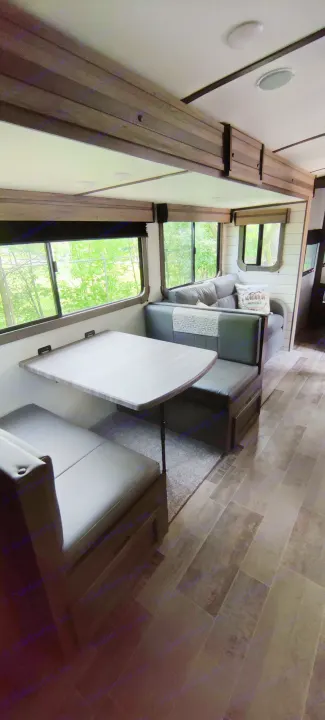 Spacious, modern RV rental interior featuring a dining booth, comfortable sofa, and large windows with green outdoor views.. Crossroads RV Sunset Trail Super Lite 2021