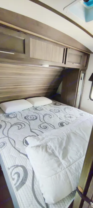Cozy RV rental bedroom with patterned mattress, white comforter, two pillows, and overhead storage cabinets.. Crossroads RV Sunset Trail Super Lite 2021
