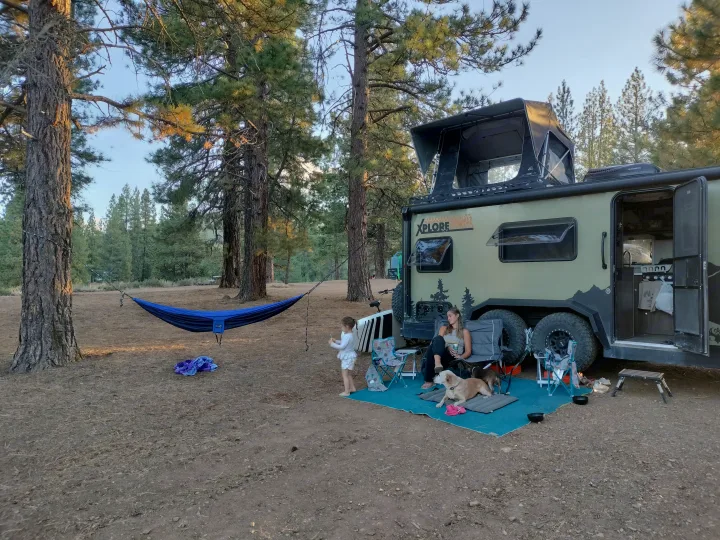 Family enjoys their XPLORE RV rental campsite setup with hammock & dogs among pine trees.. Xplorer X22 2022
