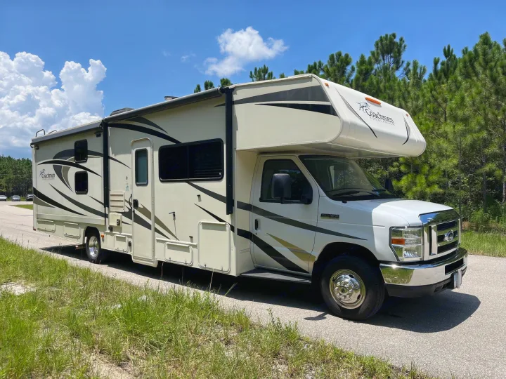 White Coachmen Freelander RV rental parked roadside. Perfect for your next adventure under blue skies with fluffy clouds & tall pines.. Forest River Coachmen Freelander 2018