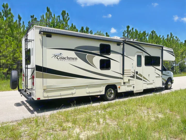 Coachmen Freelander RV rental, a motorhome, parked on a sunny road beside pine trees. Ready for your next outdoor travel.. Forest River Coachmen Freelander 2018