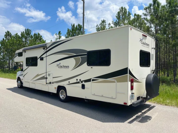 A cream-colored Coachmen Freelander RV rental parked on an asphalt road under a blue sky with pine trees.. Forest River Coachmen Freelander 2018