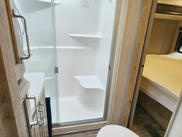 Clean RV rental bathroom showcasing a white shower, vanity, and a view into the bright bedroom with bed.. Keystone Avalanche 2021