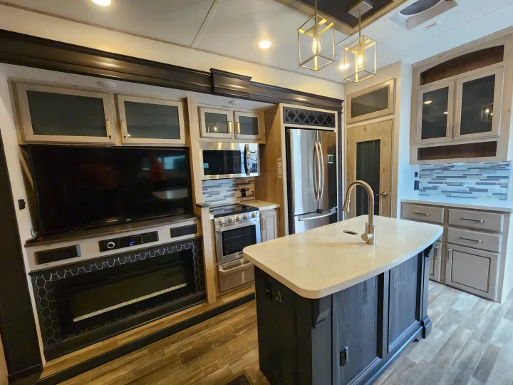 Experience comfort in this modern RV rental kitchen, featuring an island, stainless appliances, TV, and a cozy fireplace.. Keystone Avalanche 2021