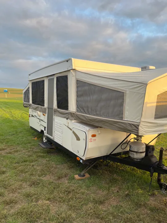 This pop-up camper, ideal for an RV rental, is set up on a grassy field with canvas extensions & a visible propane tank.. Forest River Rockwood Premier 2009