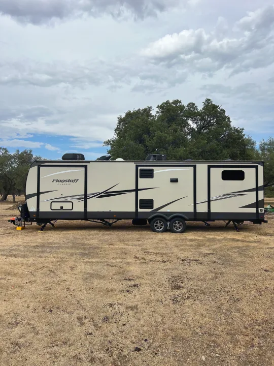 This Flagstaff Classic RV rental is parked on a dry field under cloudy skies, ready for your next outdoor adventure.. Forest River Flagstaff Classic 2022