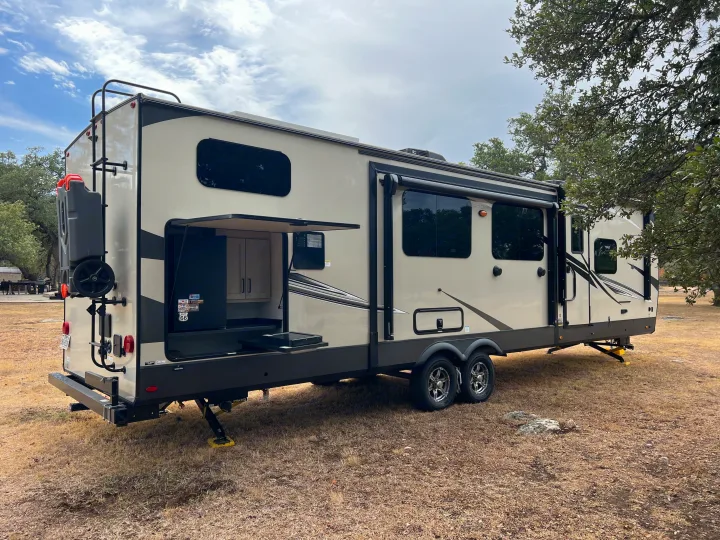 Spacious RV rental travel trailer with an open outdoor kitchen, parked at a campsite on dry grass. Ready for adventure!. Forest River Flagstaff Classic 2022
