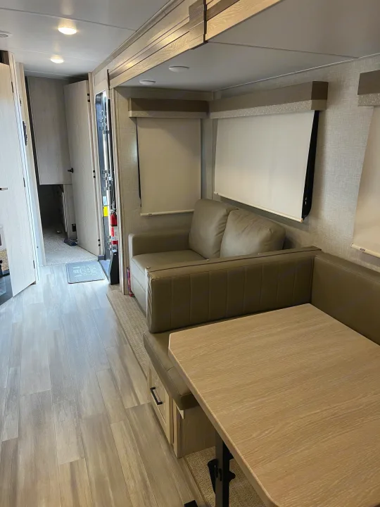 Modern RV rental interior: Light wood flooring, dinette with table, cozy sofa, and sleek window blinds. Ready for adventure.. Forest River Flagstaff Classic 2022
