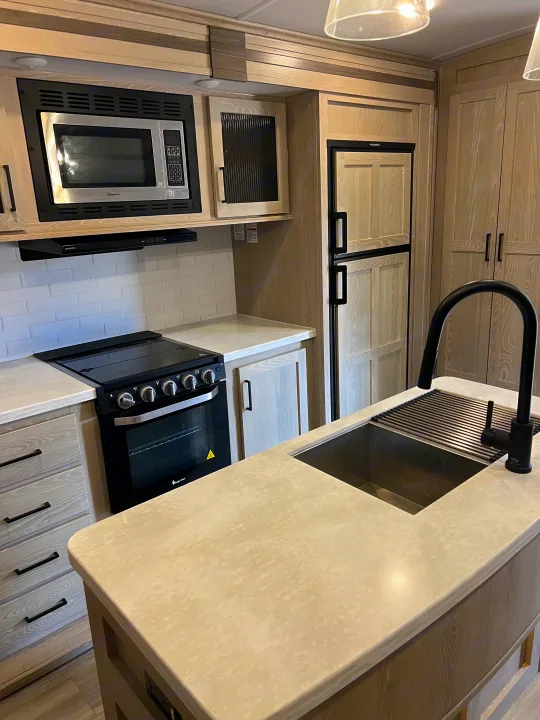 Modern RV rental kitchen featuring light wood cabinets, microwave, stove, sink, and refrigerator.. Forest River Flagstaff Classic 2022