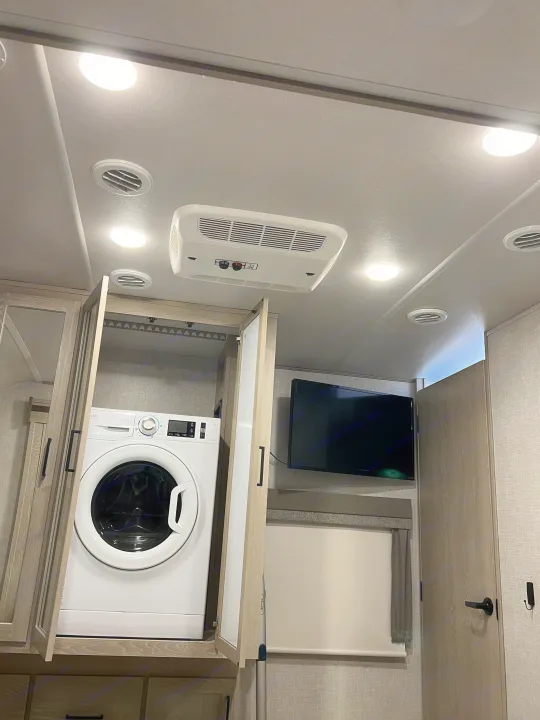 Inside an RV rental: A compact washer/dryer, wall-mounted TV, and overhead AC unit provide modern comfort.. Forest River Flagstaff Classic 2022