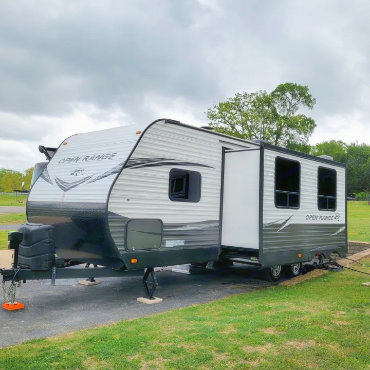 An Open Range travel trailer, ready for your next RV rental trip, is fully set up at a green, paved campsite under cloudy skies.. Highland Ridge RV Open Range Conventional OT26BHS 2019