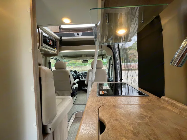 RV rental: Inside a modern camper's galley kitchen with cooktop, microwave, and view of the front cab.. Thor Scope 2023