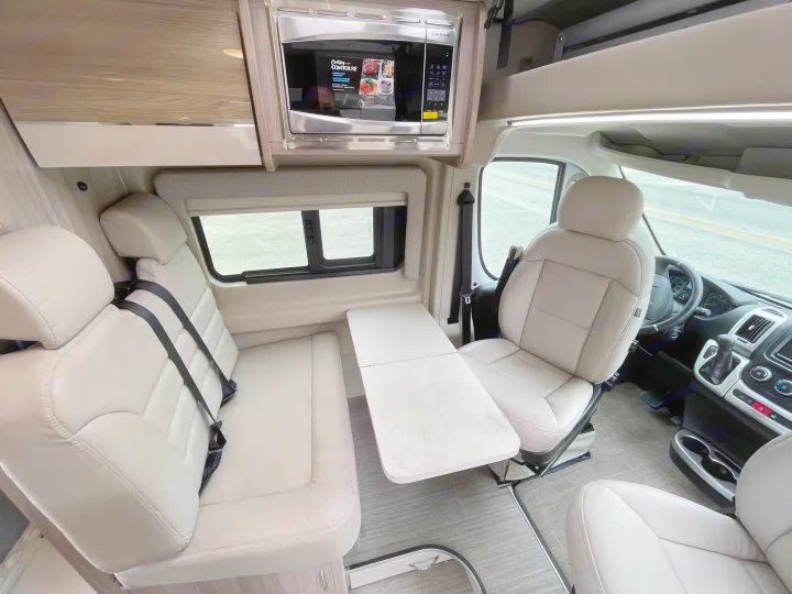 Comfortable RV rental interior: cream swivel seats, flexible table, and microwave. Driver's area joins the spacious dining zone.. Thor Scope 2023
