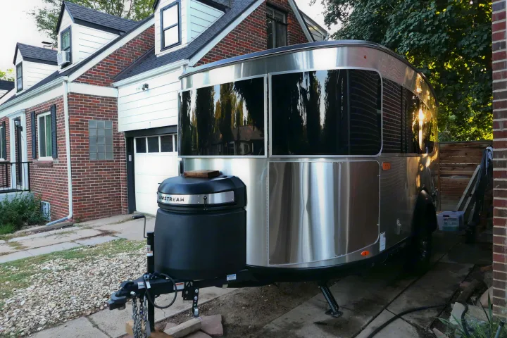 Sleek silver Airstream travel trailer, perfect for an RV rental, parked outside a brick home in sunlight.. Airstream Basecamp 2023
