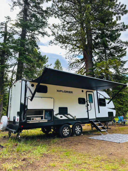 A modern XPLORER RV rental fully set up in a lush forest campsite, featuring an outdoor kitchen.. Riverside RV Xplorer 240BHx 2023