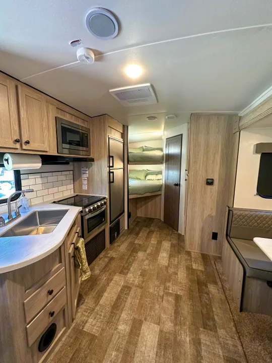Inside this modern RV rental: a light wood kitchen with stainless appliances, spacious bunk beds, and cozy dinette seating.. Riverside RV Xplorer 240BHx 2023