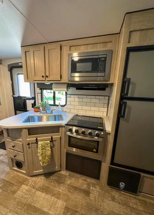 Compact and modern RV rental kitchen featuring a stainless steel microwave, stove, sink, and fridge. Ideal for road trips.. Riverside RV Xplorer 240BHx 2023