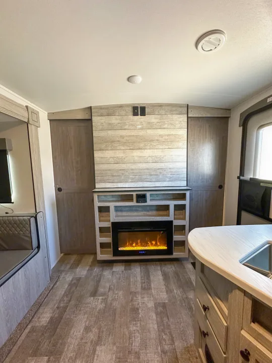 RV rental interior: A modern living space with a fireplace, shelving, kitchen counter, and dinette. Ideal for travel.. Riverside RV Xplorer 240BHx 2023