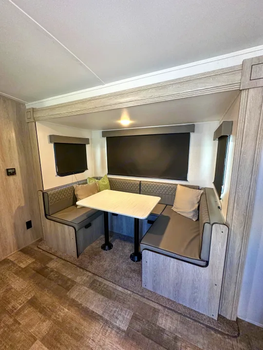 Modern RV rental dinette area with U-shaped booth seating, a table, and dark window blinds in a light wood interior.. Riverside RV Xplorer 240BHx 2023