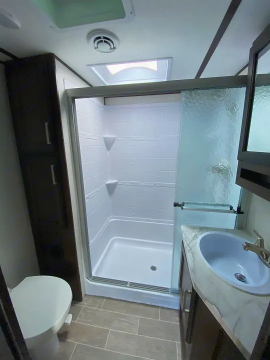 Clean RV rental bathroom featuring a sleek shower, modern sink, and a compact toilet. Perfect for travels.. Atlas Atlas Fifth Wheel 2020