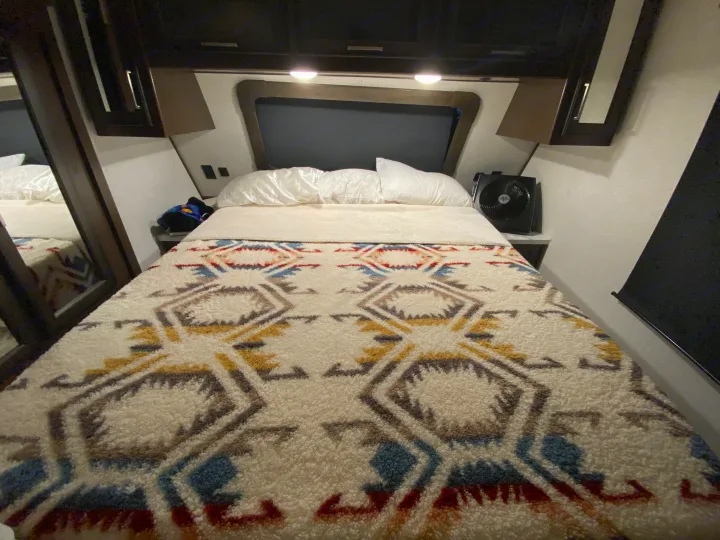 Cozy RV rental bedroom interior with a patterned blanket on the bed, overhead storage, and a small fan.. Atlas Atlas Fifth Wheel 2020