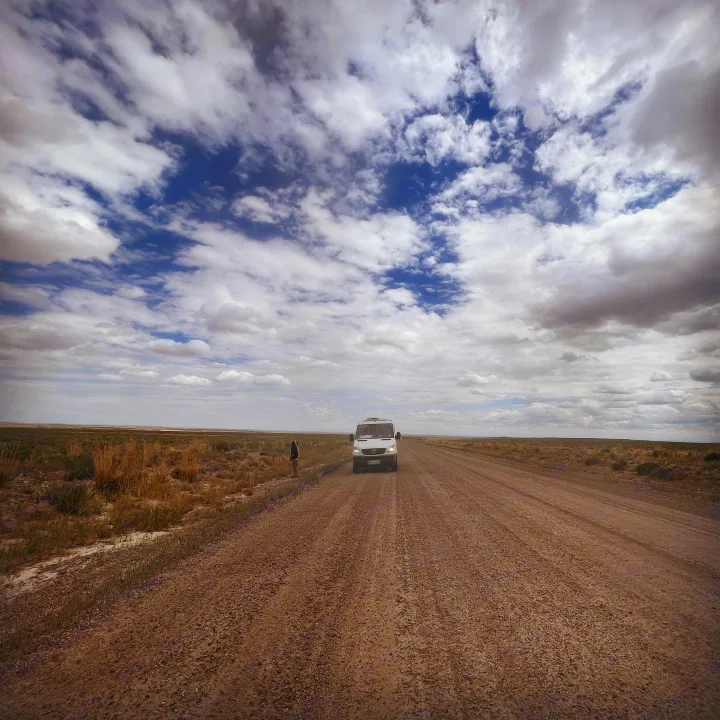 White RV rental on a remote dirt road under a dramatic sky. A person stands nearby, exploring the vast, open landscape.. Mercedes-Benz Sprinter 2012
