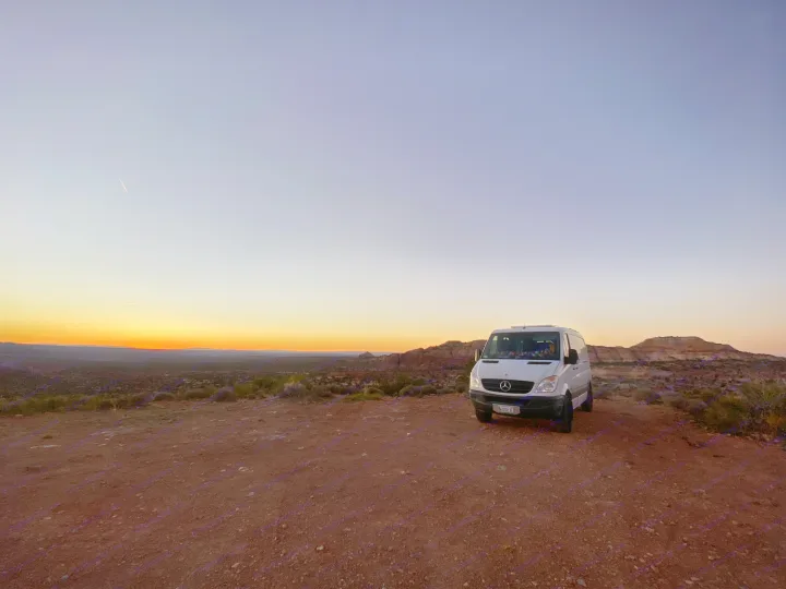 Perfect RV rental for scenic adventures! A white camper van parked on a dirt road overlooks a desert sunset.. Mercedes-Benz Sprinter 2012
