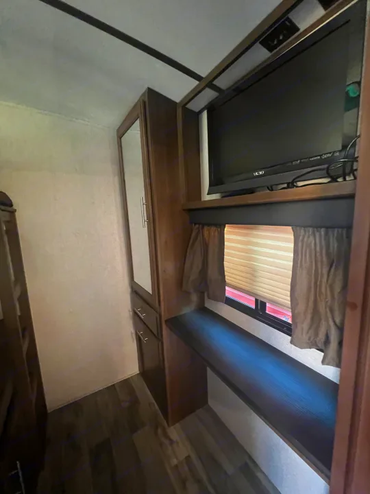 Inside an RV rental: Features a mounted TV, built-in shelf/desk, window with blinds, and mirrored storage cabinet.. Keystone RV Cougar 2019