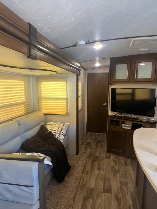 This RV rental interior shows a light-colored couch, entertainment center with TV, and wood-look flooring.. Keystone RV Cougar 2019